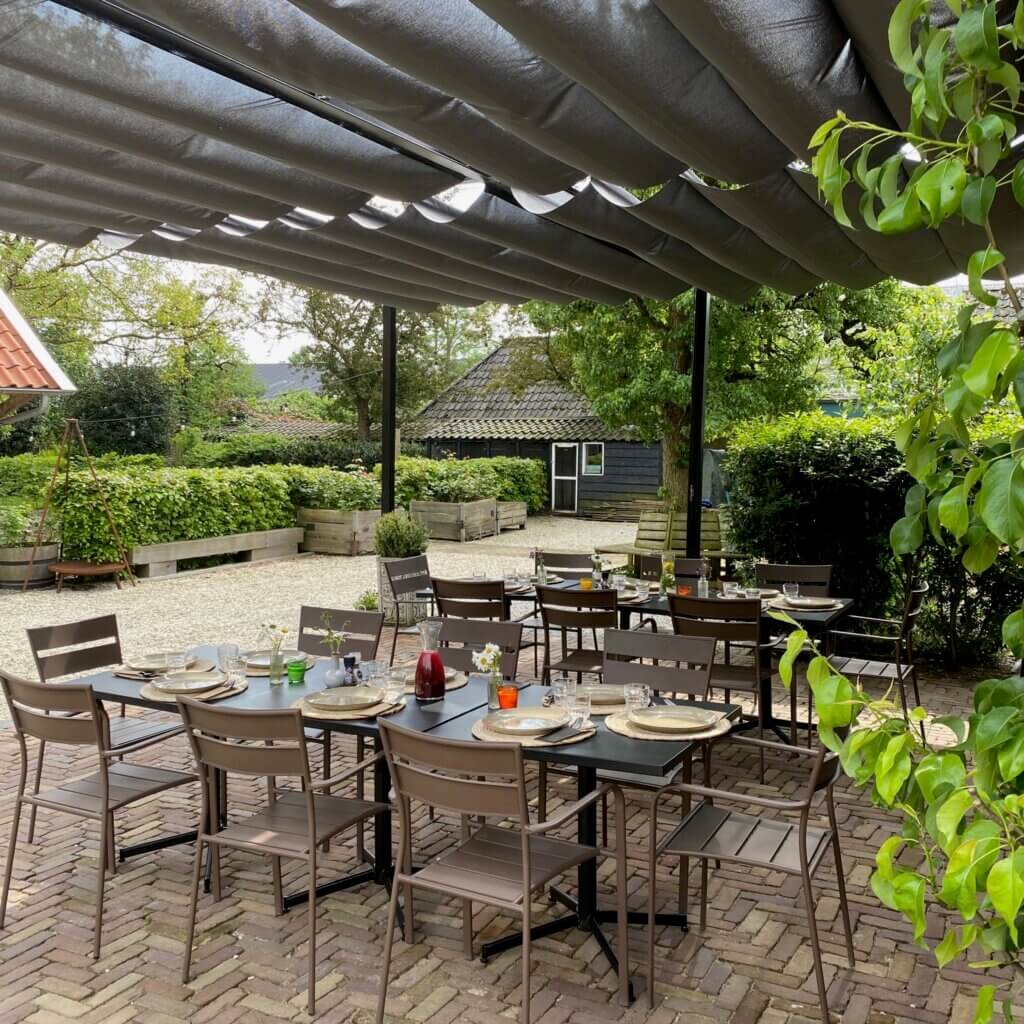 Buiten terras bij PLUK met gedekte tafels onder overkapping voor lunch of diner